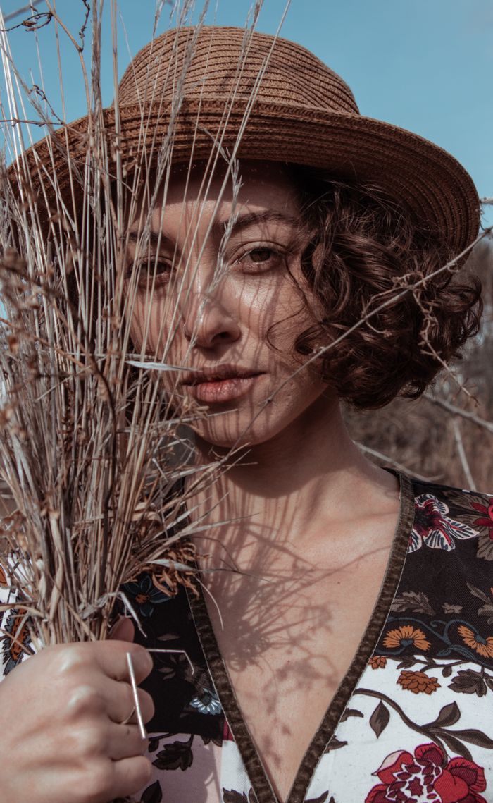 The Art of Drawing Readers In: Your attractive post title goes here A woman in a floral shirt and straw hat poses with wild grass in a natural setting.